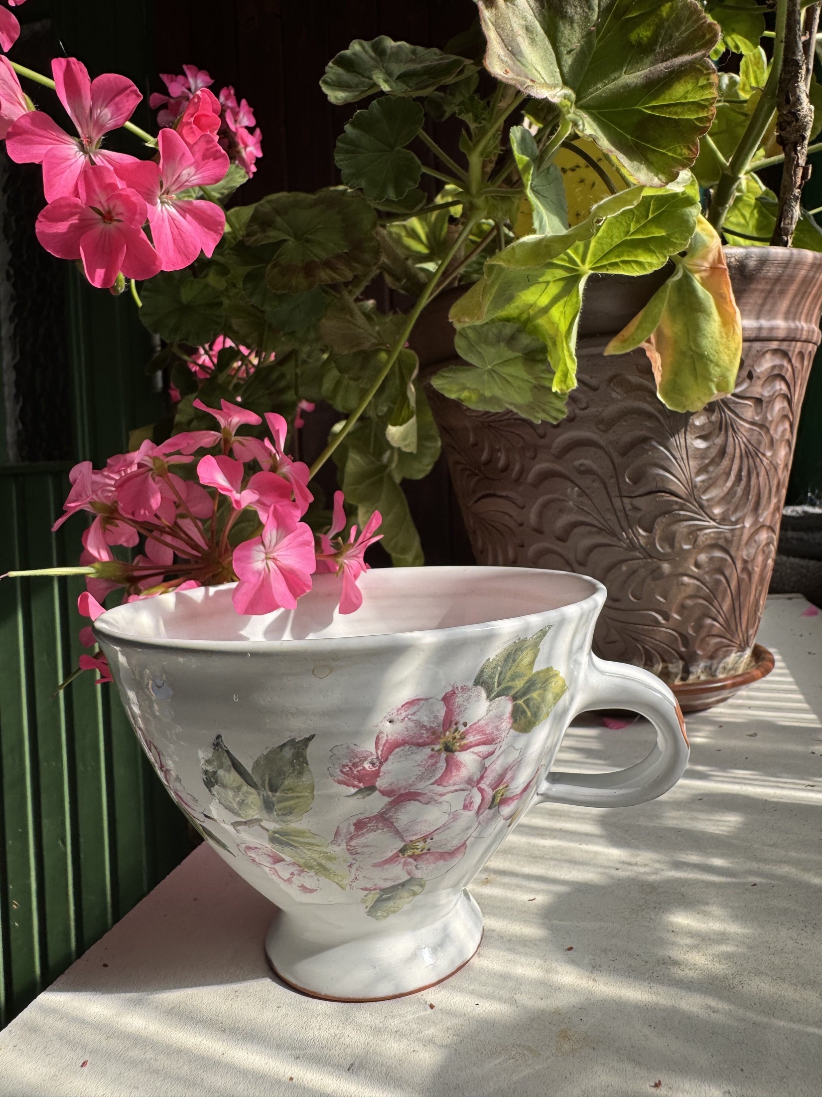 Handgjord blommig keramikkopp bland pelargoner